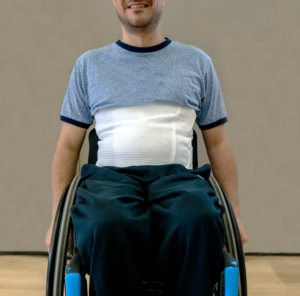 A man in a wheelchair with an abdominal binder hidden under his shirt