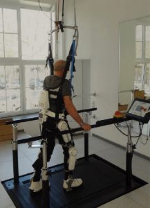 Man walking between parallel bars with his weight supported by a harness.