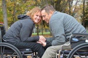 A couple in wheelchairs leaning towards each other and holding hands