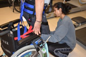 Female clinician adjusting the harness on a man sitting up out of his wheelchair
