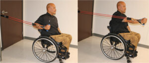Man in wheelchair using resistive band to execute a pushing movement.