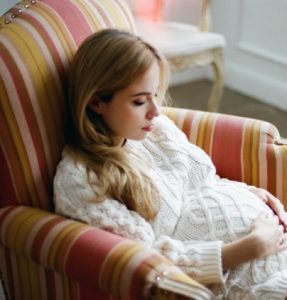 A woman sitting on a couch and holding her pregnant belly