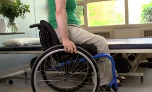 A woman lifting up her buttocks off her wheelchair by straightening her arms