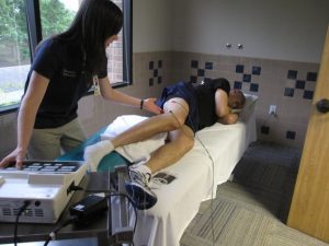 A health provider using TENS on a leg of a person who is lying down on a bed