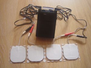 Handheld TENS unit attached by electrical wires to four self-adhesive electrodes