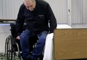 Picture showing a man transferring from his wheelchair onto a bed