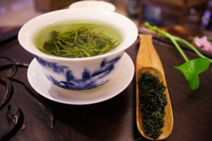 Green tea in a teacup with dry tea leaves on the side
